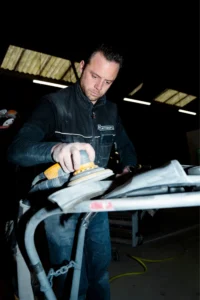 Photo d'un carrossier en train de poncer un élément de carrosserie avec une rayure profonde